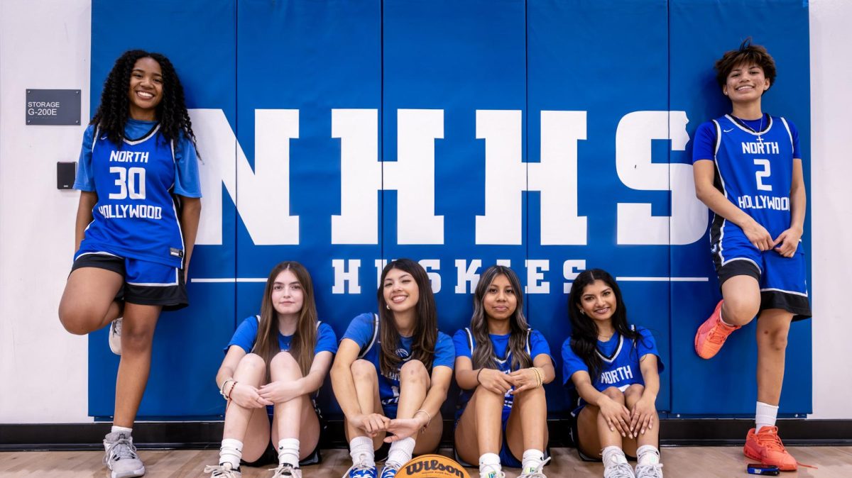 North Hollywood High School’s girls basketball team’s seniors huddle around “NHHS Huskies” logo inside of the main gym  
