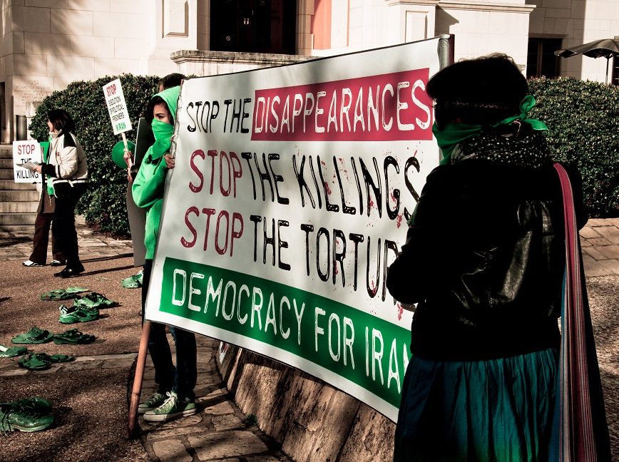 Masked women hold a sign demanding democracy in Iran. 