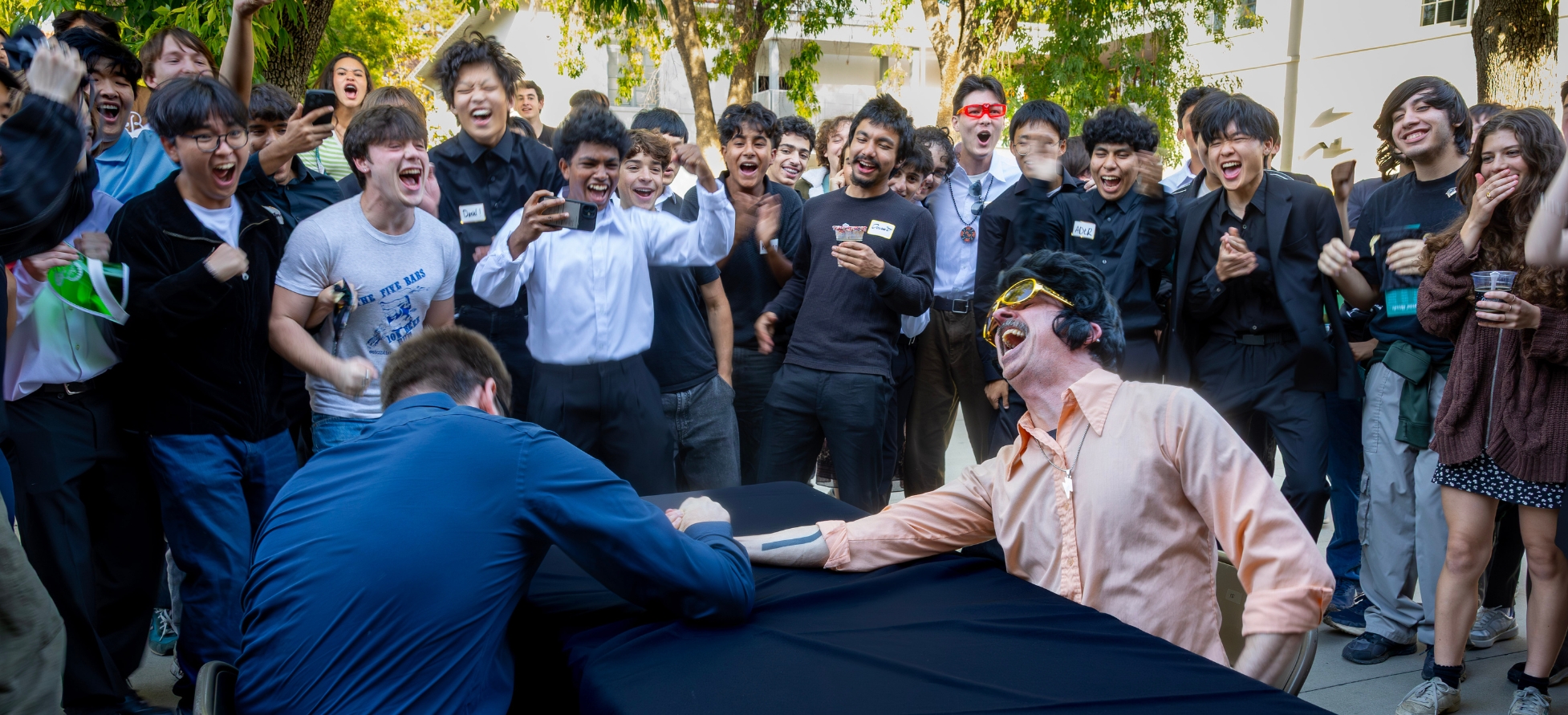 HGM Seniors gather around chuckling joyfully as they bet on who will win the arm wrestle contest, Mr. Egerdahl or Mr. Suffern.
